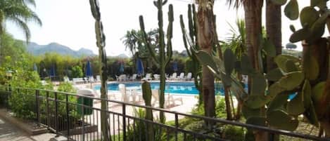 Zona de piscina con sillas de descanso y cactus, rodeada por una valla metálica.
