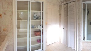 Une salle de bain avec une douche à parois de verre, une baignoire blanche et un placard de rangement avec des étagères.