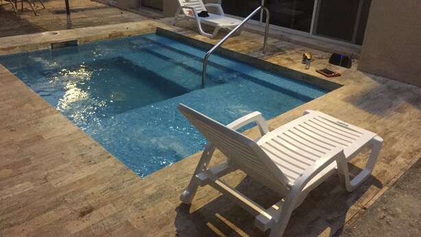 Une piscine avec deux chaises longues blanches et un escalier en métal.