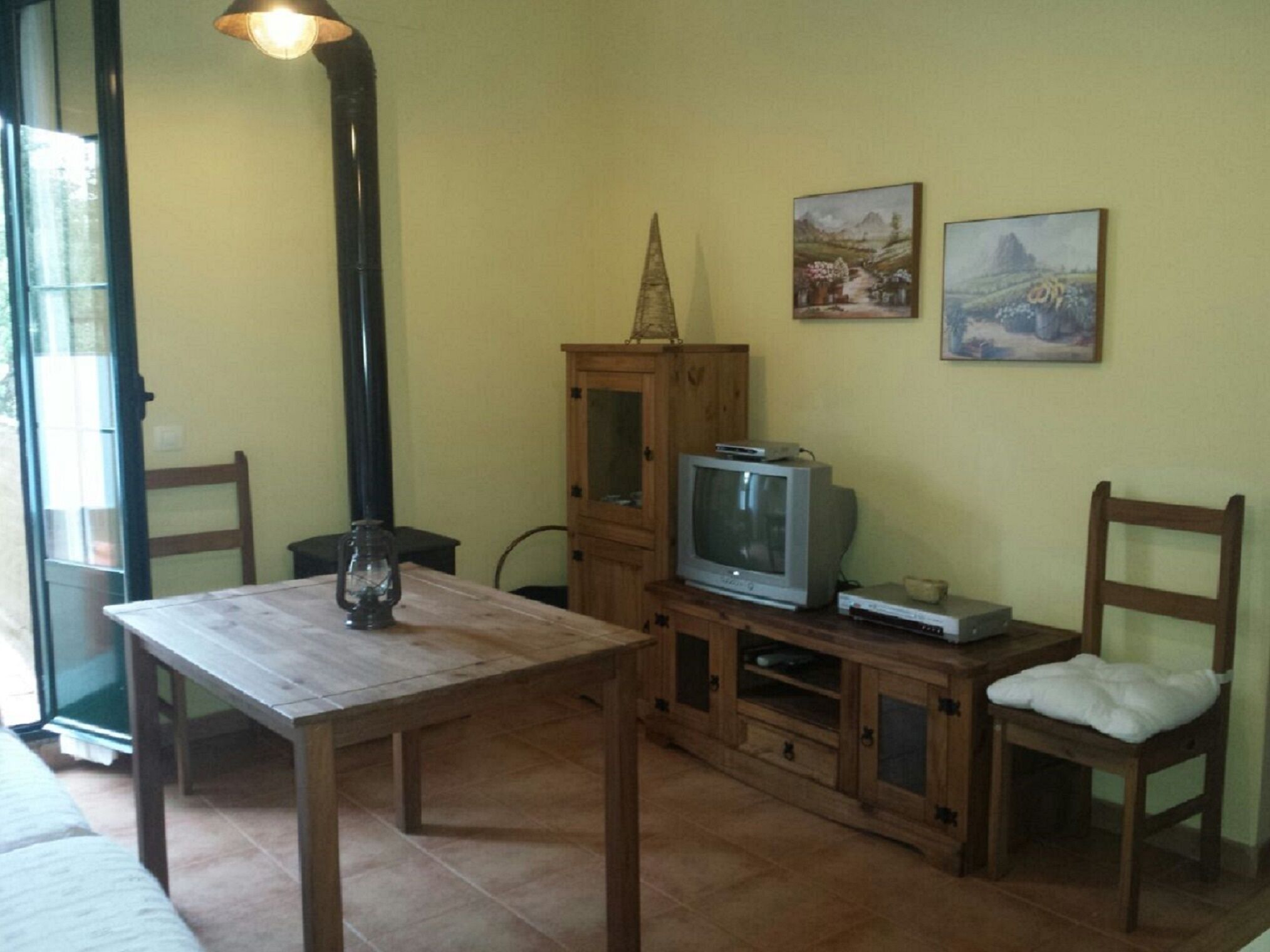 A room with a wooden table, a television on a wooden stand, and two chairs.