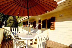 A covered outdoor patio with a table and chairs, a large umbrella, and a wooden deck.