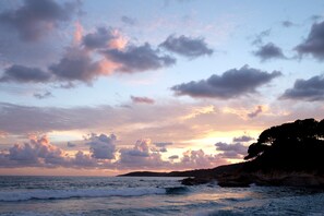 A coastal landscape with waves, a sunset, and a rocky cliff with trees.