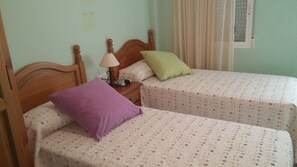 Une chambre double avec deux lits, chacun agrémenté de draps et d’oreillers à motifs floraux, une table de chevet avec une lampe et une fenêtre avec des rideaux.