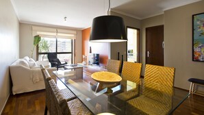 Una sala de estar moderna con una mesa de comedor de vidrio, sillas de mimbre, un sofá blanco y una lámpara colgante negra.