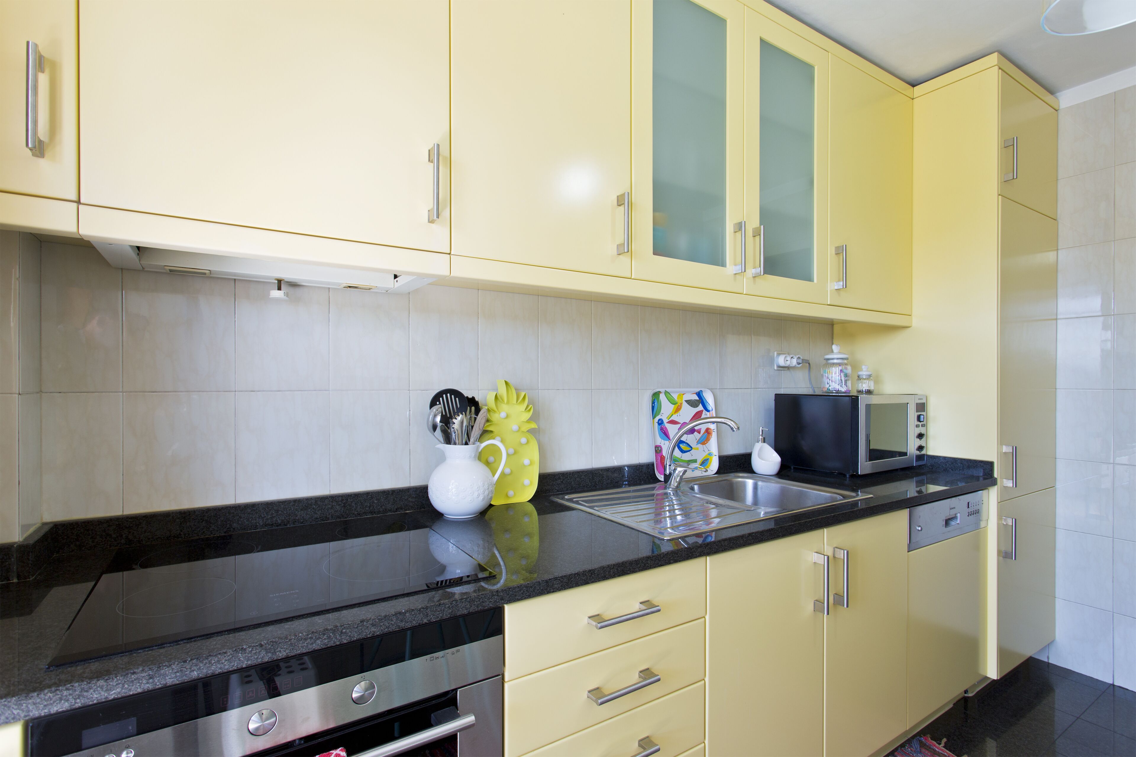 A kitchen with yellow cabinets, a black countertop, stainless steel appliances, and a microwave.