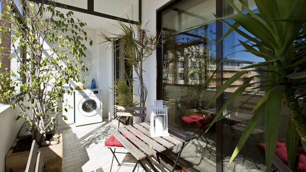 Un patio al aire libre moderno con una mesa de madera, un farol blanco y plantas en macetas.