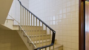 Una escalera con barandales blancos y escalones color beige, que conduce a una puerta de madera.