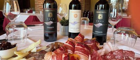 A table with three bottles of Chianti wine, a variety of cured meats, and cheese.