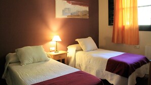 A room with two beds, a nightstand with a lamp, a painting on the wall, and a window with curtains. - Rural apartment Aptos. Rural Tourism Las Maravillas for 5 people (Jaén)