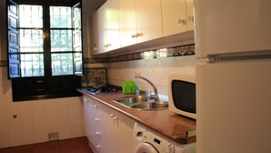 A kitchen with white cabinets, a washing machine, a sink, and a window with a view of trees. - Rural apartment Aptos. Rural Tourism Las Maravillas for 5 people (Jaén)