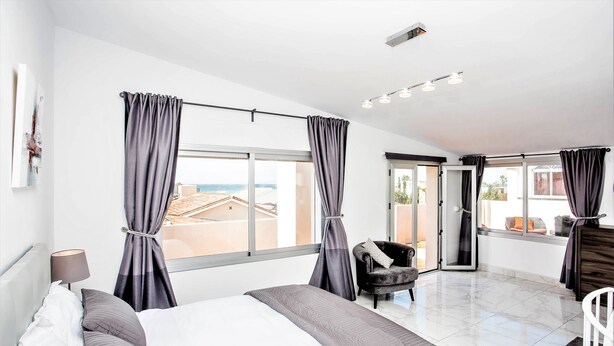 Habitació d'hotel moderna amb un llit gran, una cadira i vista a la platja.