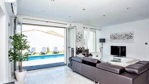 Un saló modern amb un sofà gran, una televisió i vista a una piscina.