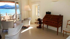 A room with a view of the sea, a wooden dresser, a chair, a lamp, and a table with a bottle. - L'île-Rousse with its feet in the water (L'Île-Rousse)