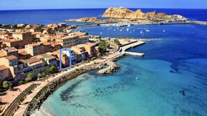 An aerial view of a coastal town with buildings, a marina, and clear blue waters. - L'île-Rousse with its feet in the water (L'Île-Rousse)