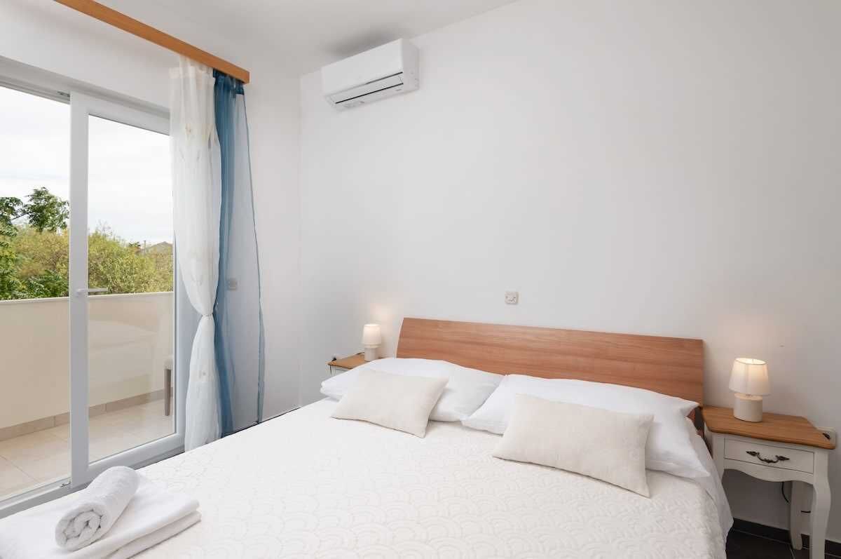 Une chambre d’hôtel avec un lit, une table de chevet avec une lampe, une fenêtre avec des rideaux et un appareil de climatisation fixé au mur.