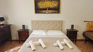 A neatly made bed with rolled towels, a headboard, bedside tables, and a painting on the wall.