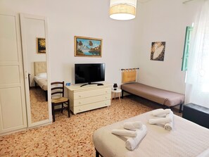 Ein Hotelzimmer mit einem Bett, einem Fernseher, einem Schreibtisch, einem Stuhl und Kunstwerken an den Wänden.