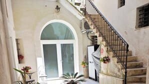 A courtyard with a bench, potted plants, a staircase, and a door leading to a building.