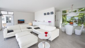 A modern living room with a white sectional sofa, a small round table with a red vase, and a TV on a white cabinet. - Wonderful Casa El Balcon Grande in La Orotava (La Orotava)