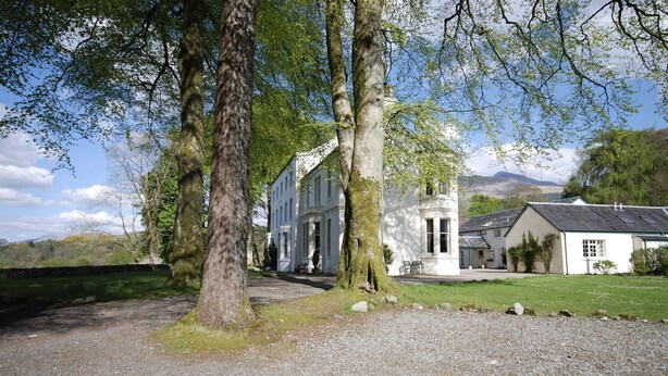 A traditional white building with a gravel driveway, surrounded by trees and a grassy area. - Elegant first floor apartment for 2 people, with great views of mountains.  (Taynuilt)
