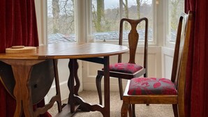 A corner room with a bay window, a wooden table, two chairs, and a carpeted floor. - Elegant first floor apartment for 2 people, with great views of mountains.  (Taynuilt)