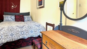 A bedroom with a bed, a wooden dresser, a mirror, and a red curtain. - Elegant first floor apartment for 2 people, with great views of mountains.  (Taynuilt)