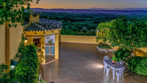 Eine Terrasse mit Tisch und Stühlen, umgeben von Grünpflanzen und Blick auf die Landschaft.