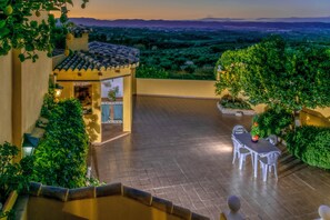 Eine Terrasse mit Tisch und Stühlen, umgeben von Grünpflanzen und Blick auf die Landschaft.
