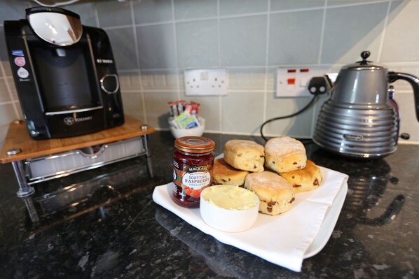 Eine Küchenarbeitsplatte mit einer Kaffeemaschine, einem Marmeladenglas und einem Teller mit Scones.