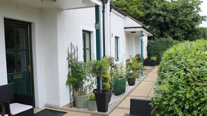 Un bâtiment blanc avec des bordures vertes, des sièges à l’extérieur et des plantes en pot.