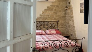 A bedroom with a stone wall, a bed with a metal frame, a hanging light fixture, and a ceiling fan. - Apartment Nikolina house in center of the old town Trogir (Trogir)