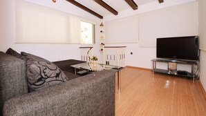A living room with a sofa, a TV on a stand, a window, and a wooden floor. - Apartment Nikolina house in center of the old town Trogir (Trogir)