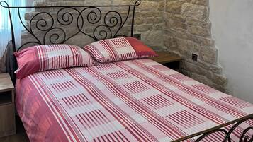 Een slaapkamer met een stenen muur, een bed met metalen frame, een nachtkastje en een wandairconditioner.