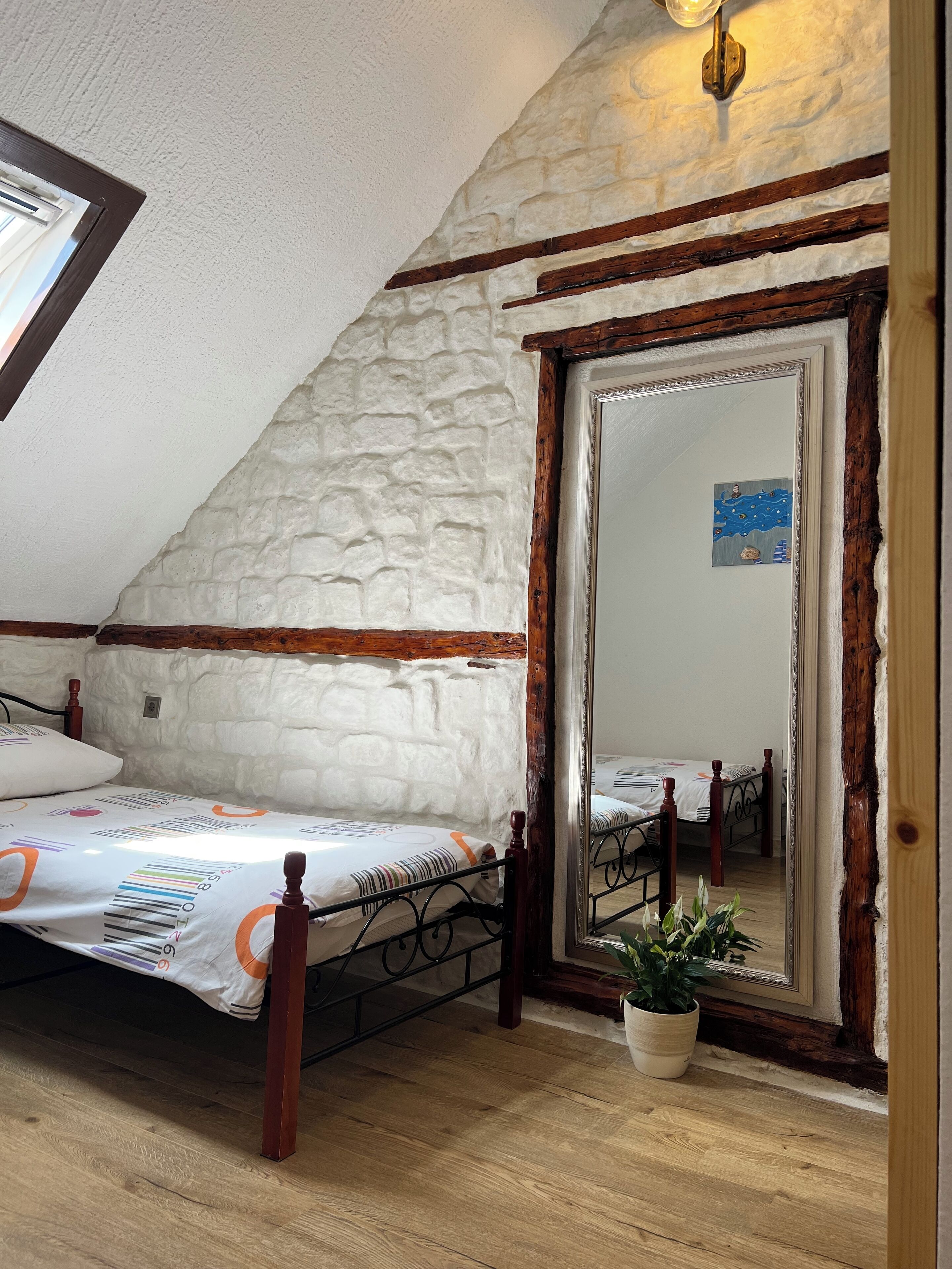 A bedroom with a sloped ceiling, a wooden bed frame, a large mirror, and a potted plant.