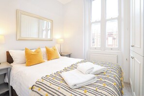 A hotel room with a bed, two bedside lamps, a window, and a radiator.