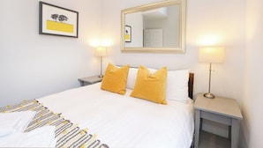 Quarto de hotel com uma cama, duas luminárias de cabeceira, um espelho e um quadro na parede.