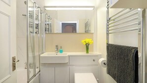 Casa de banho com cabine de chuveiro em vidro, lavatório branco, sanita e porta-toalhas.