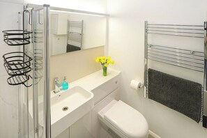A bathroom with a glass shower enclosure, a white sink with a mirror above it, a toilet, and a towel rack with a towel.