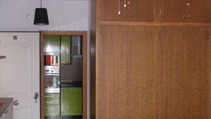 A room with a wooden wardrobe, a white door, and a green kitchen area with cabinets and a stove. - Magnificent Penthouse in Barbate (Barbate)