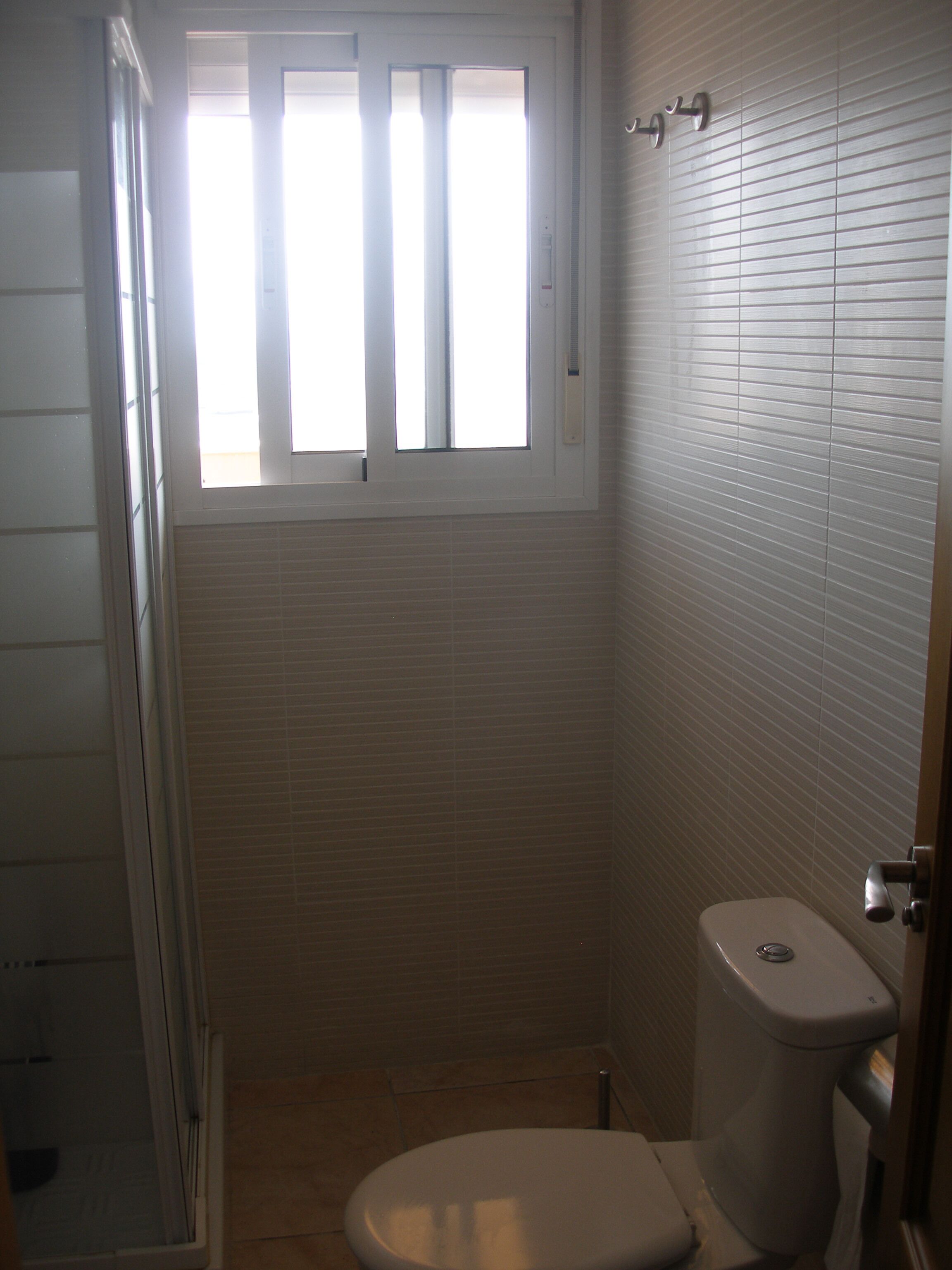 Une petite salle de bain propre, équipée de toilettes, d’une fenêtre et d’un espace douche.