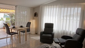 Een moderne woonkamer met een eethoek, met een bank, twee fauteuils, een salontafel en een eettafel met stoelen.