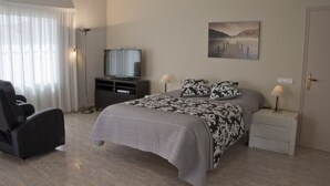 Een slaapkamer met een bed, een televisie, een stoel, een nachtkastje en een schilderij aan de muur.