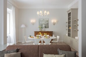A dining area with a chandelier, white chairs, a round table, and a cabinet with shelves. - Spacious and stylish Embassy Loren flat (Roma)
