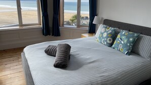 Un dormitorio con una cama grande, vista a la playa y una ventana con cortinas.