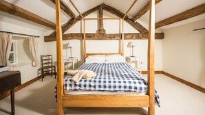 Ein Schlafzimmer mit Himmelbett, Holzbalken, Schreibtisch und Stuhl.
