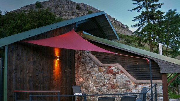 Eine Holzhütte mit Steinwand, Whirlpool und zwei Stühlen unter einer roten Markise.