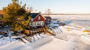 A red wooden house with a porch and a wooden bridge over a frozen lake.