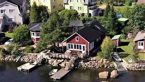 A waterfront property with a dock, a red house, and surrounding greenery.