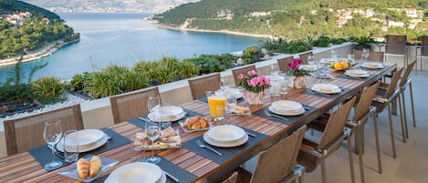 A dining table set with plates, glasses, and croissants, overlooking a scenic coastal view.