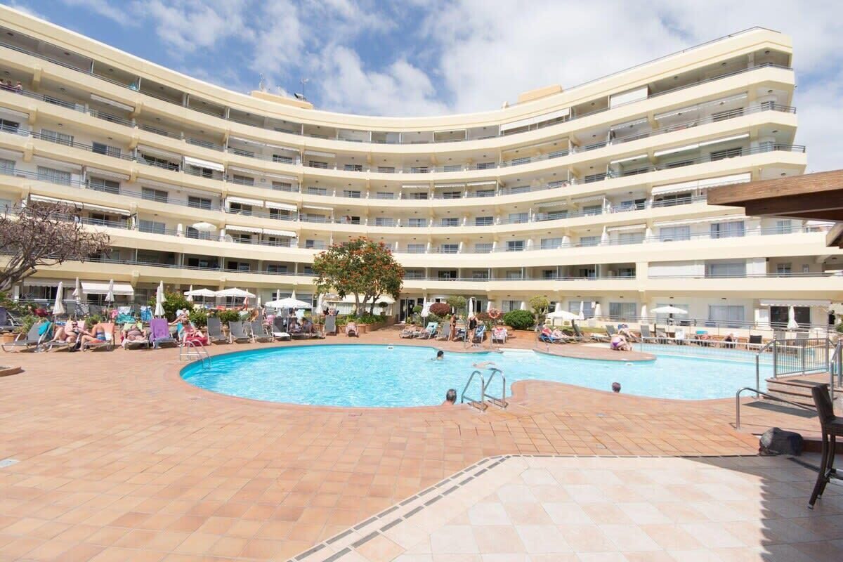 A multi-story hotel with a central swimming pool surrounded by sun loungers and umbrellas.